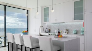 A modern kitchen with a large island, bar stools, and a view of the sea.