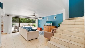 Un vaste espace de vie doté d’une grande fenêtre, d’un ventilateur de plafond et d’un escalier menant à un niveau supérieur.