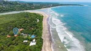 Une vue aérienne d’une zone côtière avec une plage, une végétation luxuriante et quelques bâtiments.