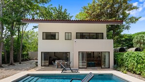 Un bâtiment moderne à deux étages doté d’une piscine, d’un espace extérieur aménagé et d’une végétation luxuriante.