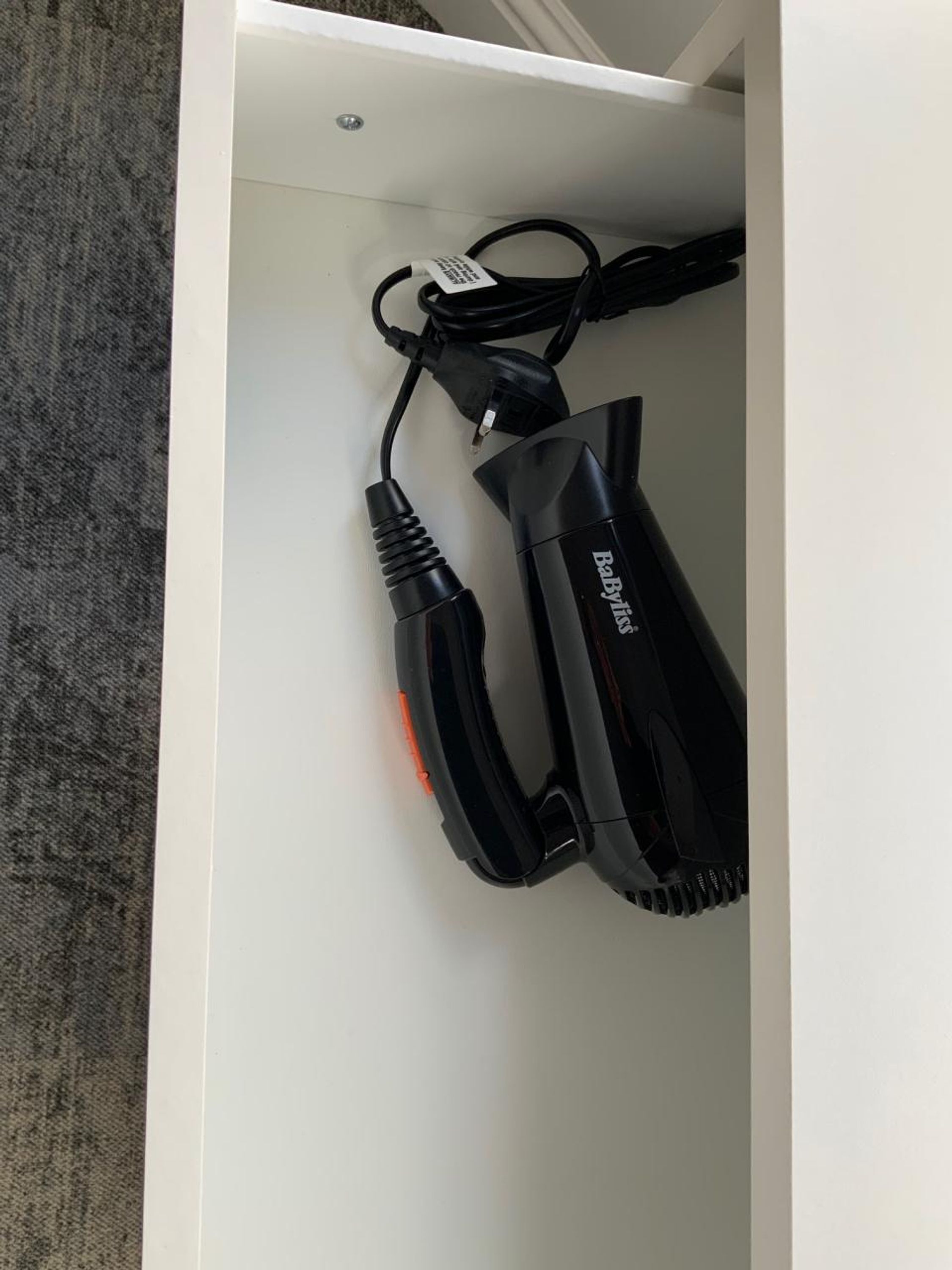 A white drawer containing a black hair clipper with a cord.