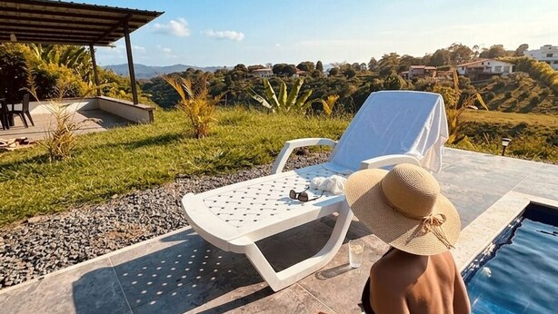 A poolside area with a lounge chair, a person wearing a hat, and a clear view of the surrounding landscape.