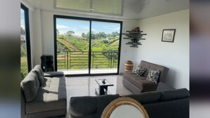 A modern living room with a large sliding glass door leading to a balcony, a grey sofa, a wicker chair, and a small table.