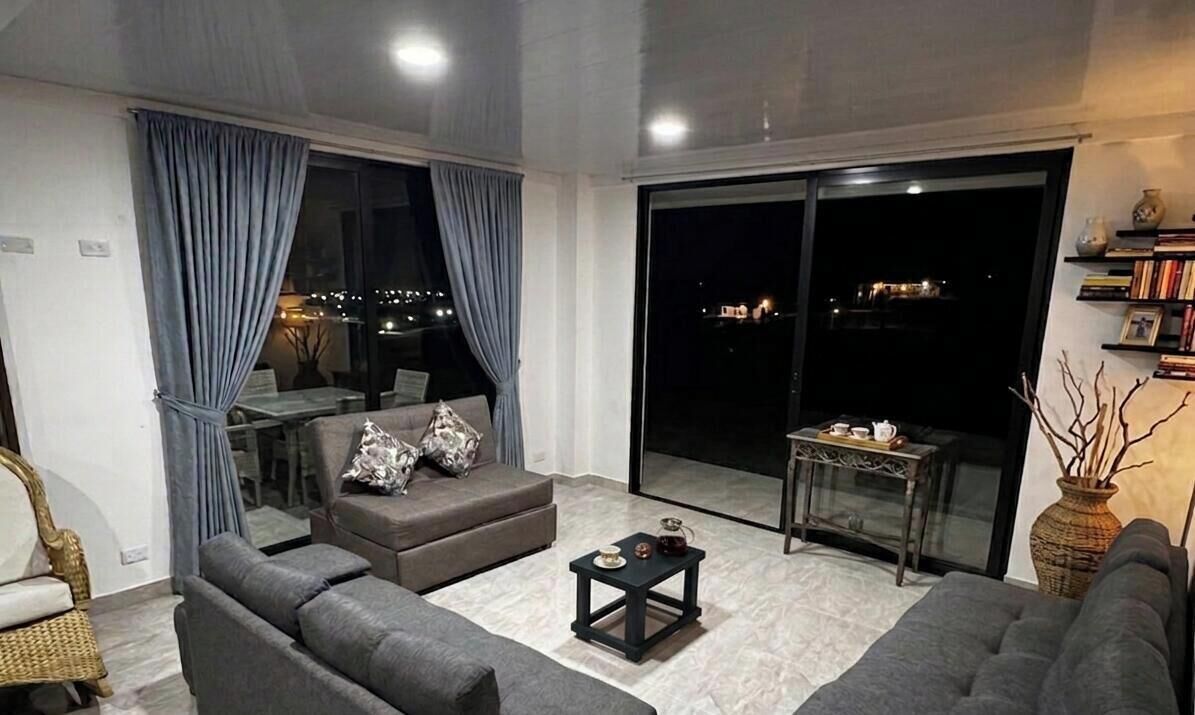A modern living room with a sofa, a small table, and a view of the city at night.