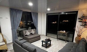 Un salon moderne avec un canapé, une petite table et une vue sur la ville la nuit.