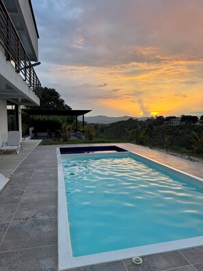 Una piscina con vistas a un atardecer y colinas al fondo.