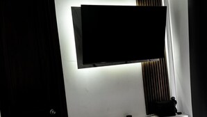 A modern room with a flat-screen TV mounted on the wall, a wooden cabinet below, and a door to the left.
