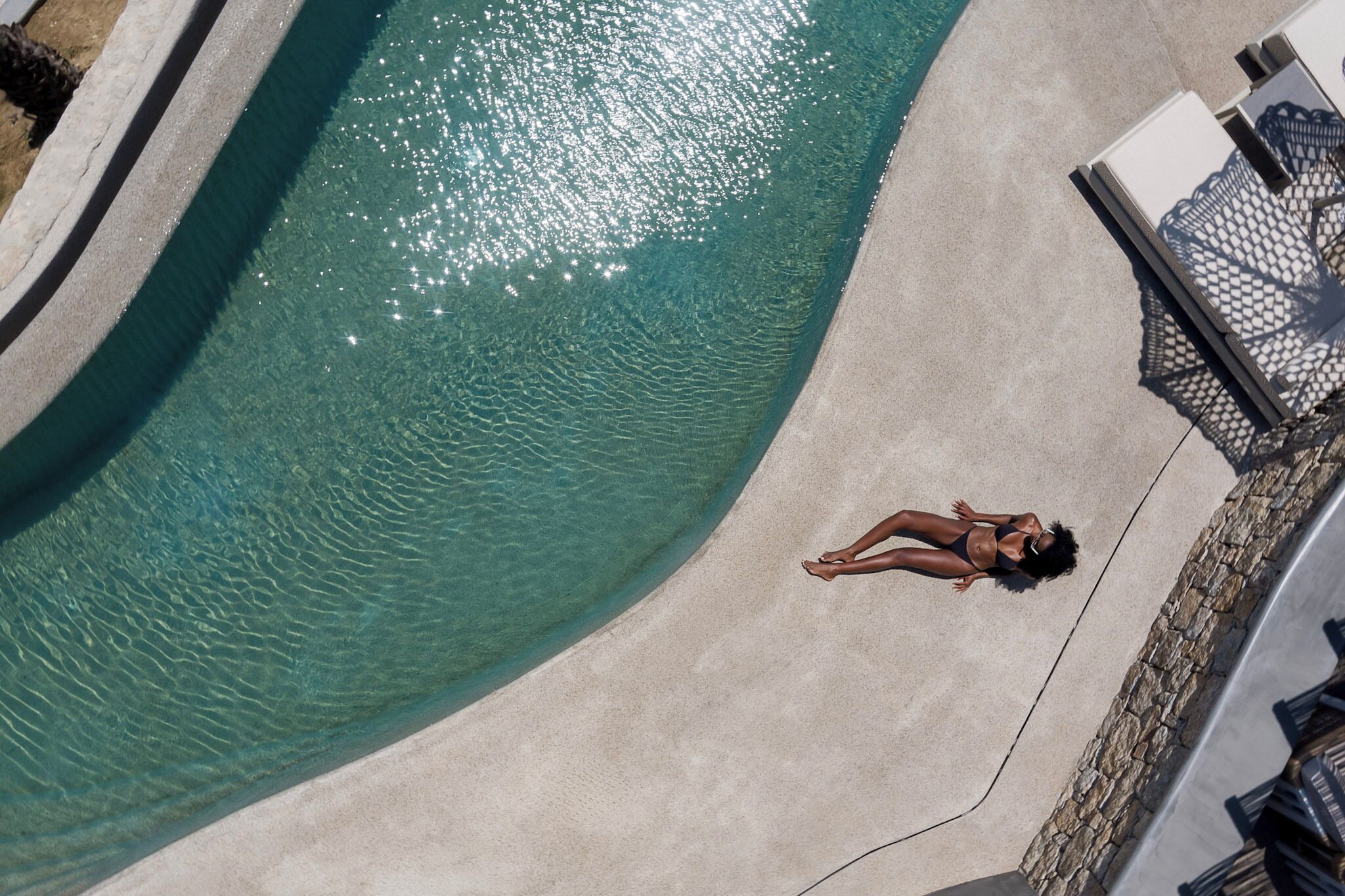 An aerial view of a swimming pool with clear water, surrounded by a concrete deck and lounge chairs.