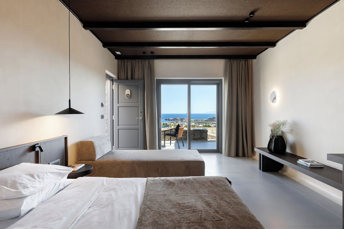 Een hotelkamer met twee bedden, een bureau, een stoel en uitzicht op zee.