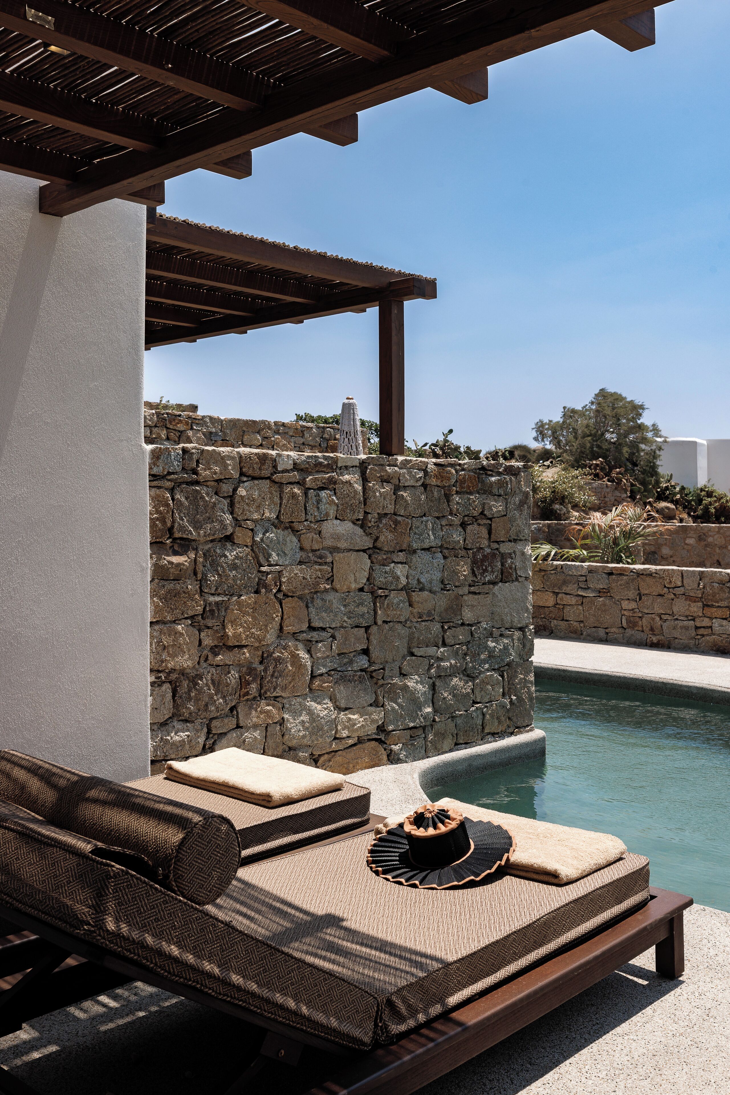 Eine Poollounge mit Mauerwerk, einer Holzpergola und Liegestühlen.