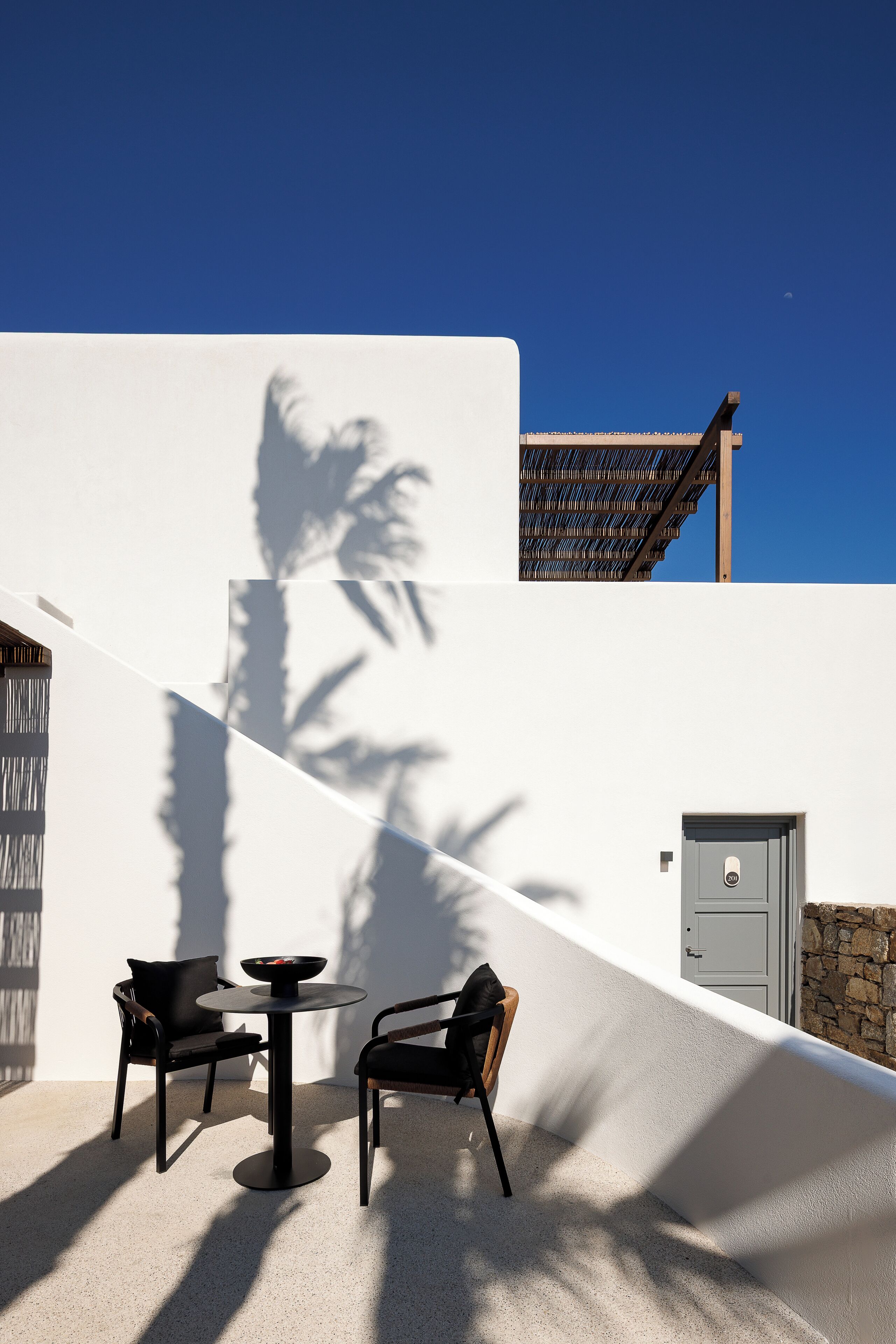 A modern outdoor seating area with two chairs and a table, a stone wall, and a door.