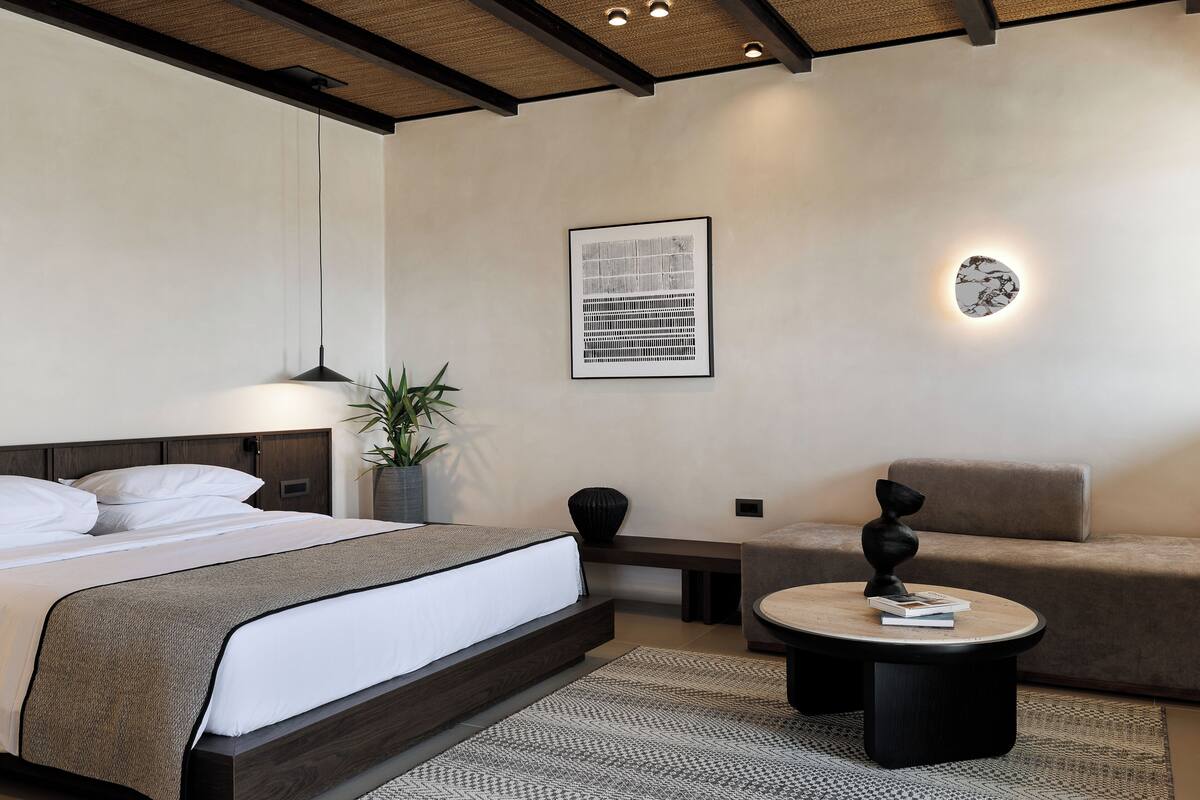Een moderne slaapkamer met een groot bed, een ronde salontafel, een bank en een wandlamp.