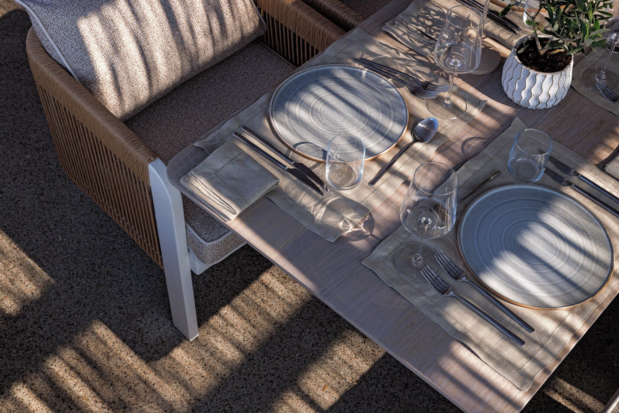 A dining table set with plates, cutlery, and glasses, with a cushion on a wicker chair.