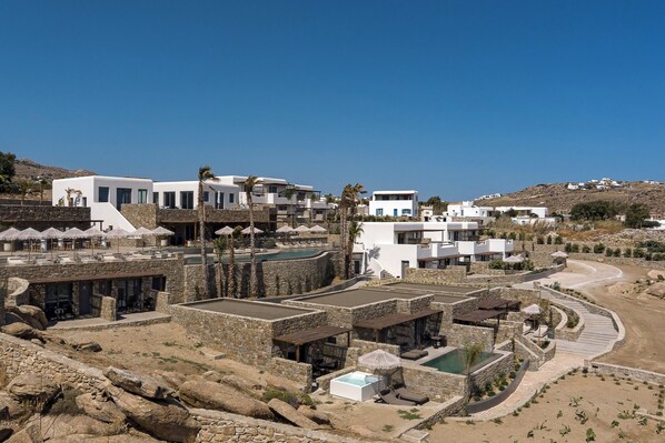 Un complejo turístico costero con edificios blancos modernos, una zona de piscina y un paisaje rocoso.