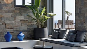 Un interior moderno con una pared de piedra, ventanas amplias, una zona de estar con cojines y una planta en maceta.