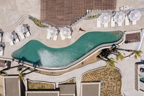 Vista aérea de un resort con piscina curvo, sillones de descanso y palmeras.
