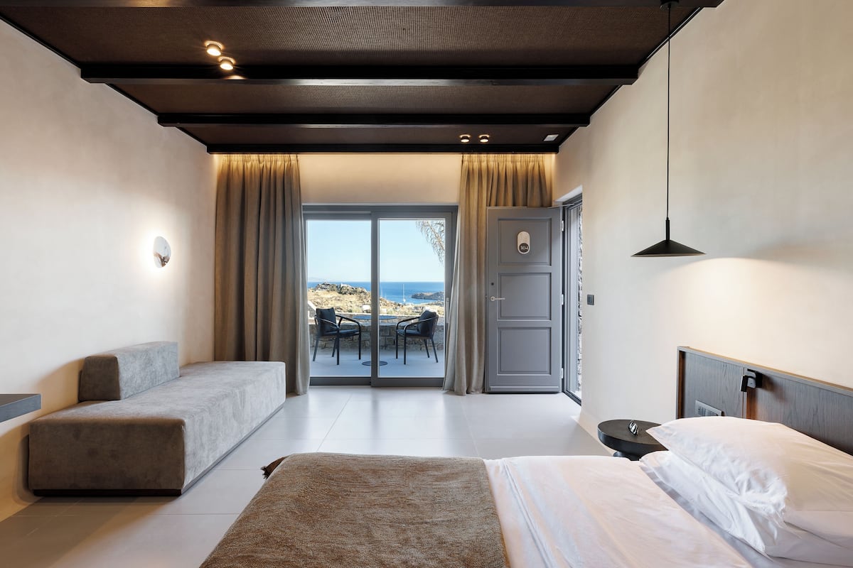 Een moderne slaapkamer met een bank, een bed en uitzicht op zee door een glazen deur.