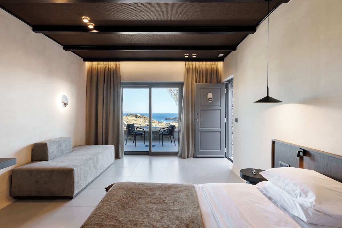 Een moderne slaapkamer met een bank, een bed en uitzicht op zee door een glazen deur.