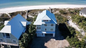 Une propriété située sur la côte, comprenant deux bâtiments principaux, offrant une vue sur la plage et un sentier sablonneux menant à la plage.