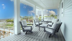 Une terrasse extérieure couverte, dotée de mobilier blanc et offrant une vue sur la plage.