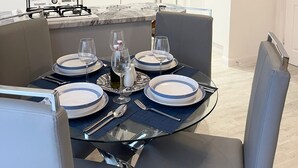 A modern kitchen with dark brown cabinets, a marble countertop, and a dining area with a glass table set for four. - The Madison Apartment (Dagenham)