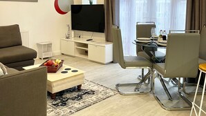 A modern living room with a flat-screen TV, a sofa, a dining table with chairs, and a chandelier. - The Madison Apartment (Dagenham)