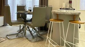 A modern kitchen with a gas stove, a built-in oven, and a stainless steel range hood. There is a dining area with a glass table and metal chairs. - The Madison Apartment (Dagenham)
