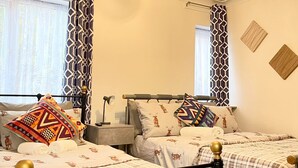 A bedroom with two beds, a nightstand, a lamp, and a ceiling light fixture. - The Madison Apartment (Dagenham)