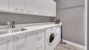 A laundry area with a washing machine, a sink, and a mop. - Sunset Lane Waterfront Home (West Vancouver)