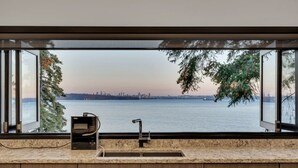 A kitchen with a large window overlooking a body of water and a distant city skyline. - Sunset Lane Waterfront Home (West Vancouver)