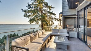 A modern outdoor living area with a sofa, a coffee table, and a grill, overlooking a body of water. - Sunset Lane Waterfront Home (West Vancouver)
