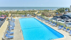 Ein Swimmingpool mit blauem Wasser, umgeben von Liegestühlen und Sonnenschirmen, mit Blick auf den Strand und den Ozean im Hintergrund.
