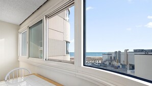 Ein Zimmer mit großem Fenster, das auf einen Strand und Industriegebäude blickt.