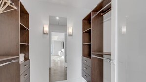 A walk-in closet with wooden shelving and drawers, a mirror, and a hallway leading to a bathroom. - Ocean City View Home (West Vancouver)
