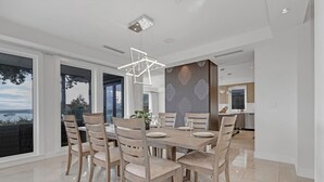 A modern dining area with a large table, six chairs, and a geometric pendant light. - Ocean City View Home (West Vancouver)
