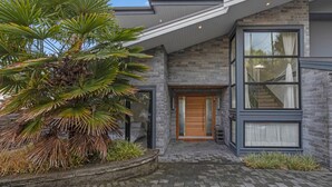 A modern house with a stone facade, large windows, and a well-maintained garden. - Ocean City View Home (West Vancouver)