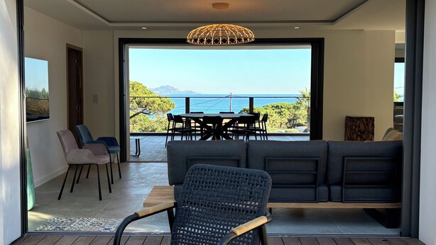 A modern living room with a large sliding glass door leading to a balcony with a view of the sea.