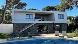 A modern two-story house with a swimming pool, outdoor seating, and a stone facade.