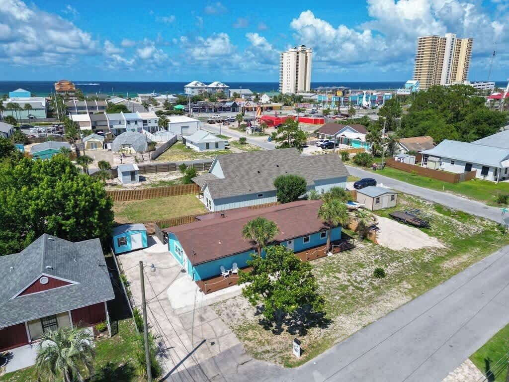 An aerial view of a residential area with houses, a small commercial area, and a beach in the background.