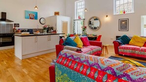 A spacious living area with a kitchen, a red sofa, and a colorful patterned throw. - 5 Star Chapel In The Heart Of North Norfolk (Dereham)