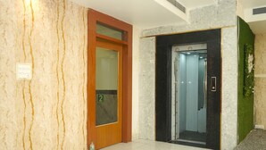 Vestíbulo de hotel con pared de mármol, puerta de madera con panel de vidrio y ascensor.