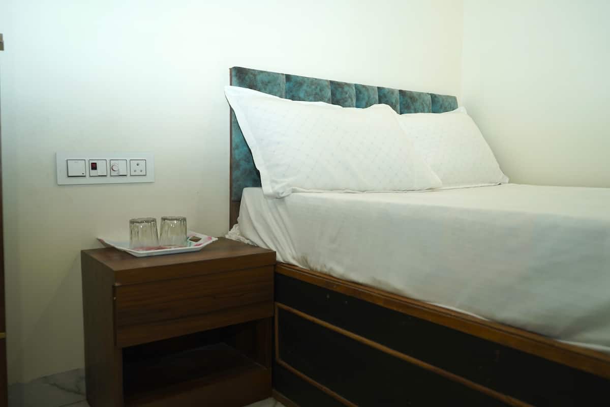 Una cama individual con cabecera de madera, una mesita de noche con una bandeja de vasos y un enchufe en la pared.