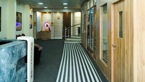 Un área de recepción con mostrador, escalera y pasillo con paneles de madera y puertas de vidrio.