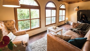 A cozy living room with a fireplace, comfortable seating, and large windows offering a view of the outdoors. - Landhaus & Lodges by Bollants (Bad Sobernheim)