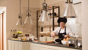 A chef preparing food in a modern kitchen with hanging pendant lights, a buffet setup, and a wine display. - Landhaus & Lodges by Bollants (Bad Sobernheim)