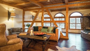 A spacious living room with wooden beams, a leather armchair, a sofa, and a coffee table with apples and a candle. - Landhaus & Lodges by Bollants (Bad Sobernheim)