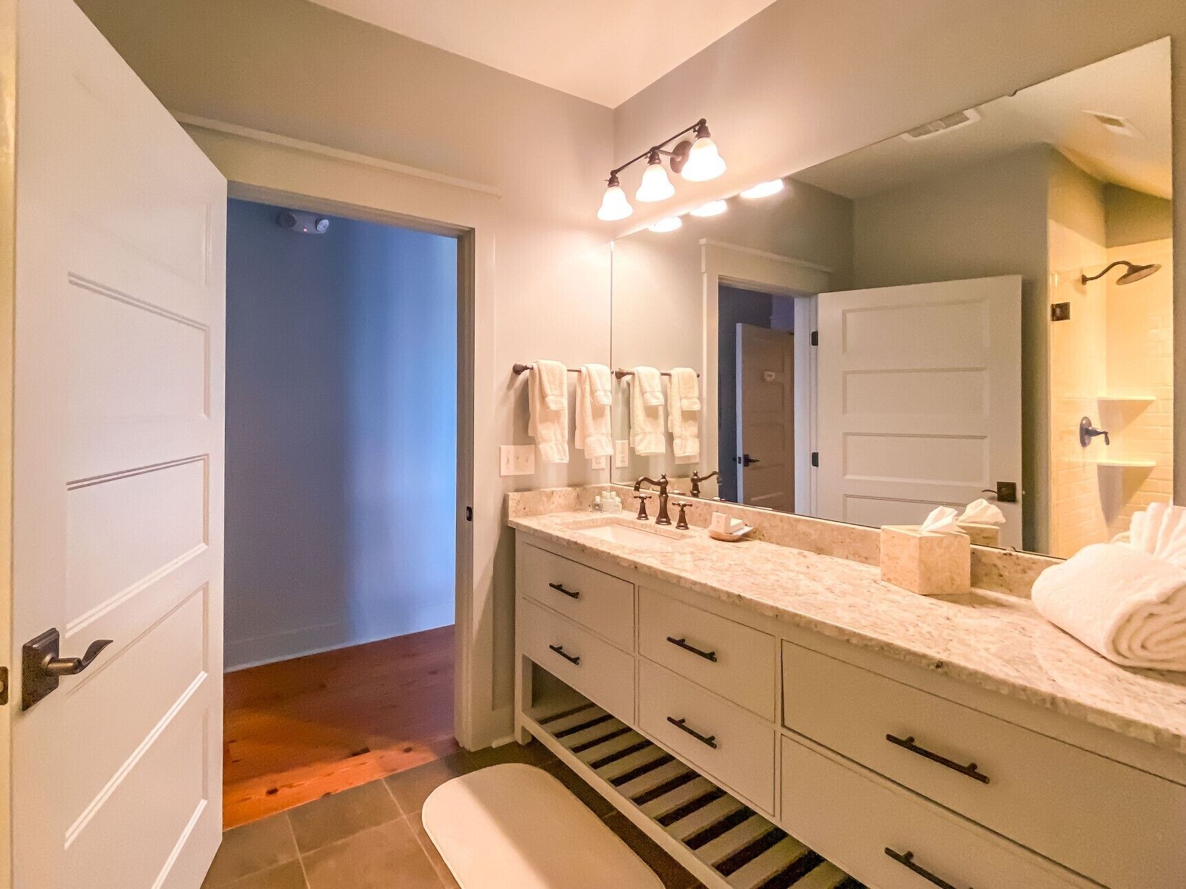 A modern bathroom with a large mirror, white vanity, and a walk-in shower.