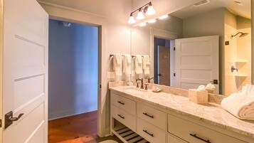 A modern bathroom with a large mirror, white vanity, and a walk-in shower.