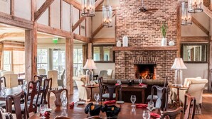 A dining area with a brick fireplace, wooden beams, and modern pendant lighting. - Blue Heron Suite w/King Bed, ADA - River Dunes (Oriental)