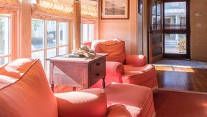 A cozy room with wooden walls and a large window, featuring a desk with a lamp, two plush armchairs, and a framed picture on the wall. - Hinkley Cottage, Quaint w/Queen Bed – River Dunes (Oriental)